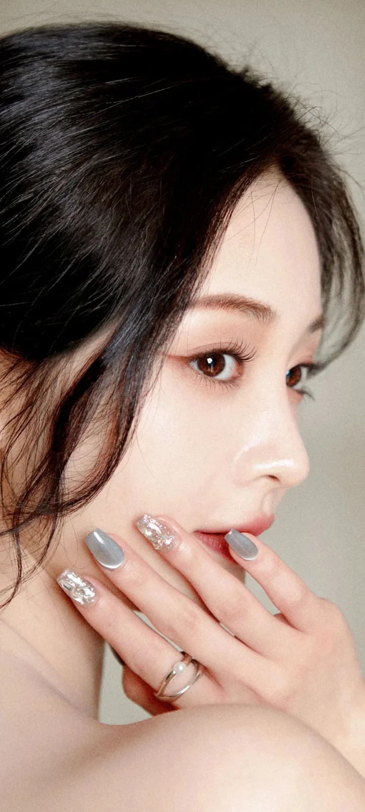 一名女性以侧脸近距离面对镜头，手指轻触嘴唇，呈现精致妆容与美甲。
