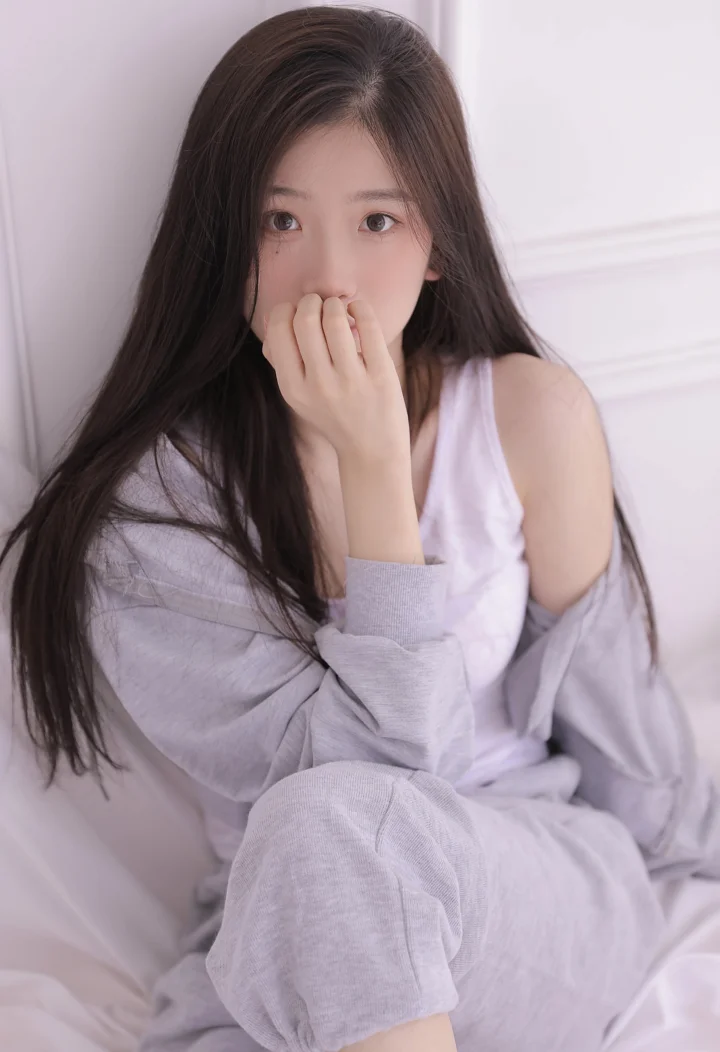 一名长发女性坐在室内，以柔和的浅色调面对镜头。