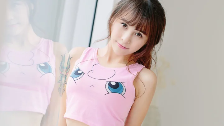一名微笑的女性穿着粉色卡通图案上衣站在镜子旁，画面中可见她的倒影。