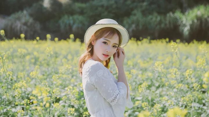 一名戴着遮阳帽的女子站在盛开的小黄花田中。