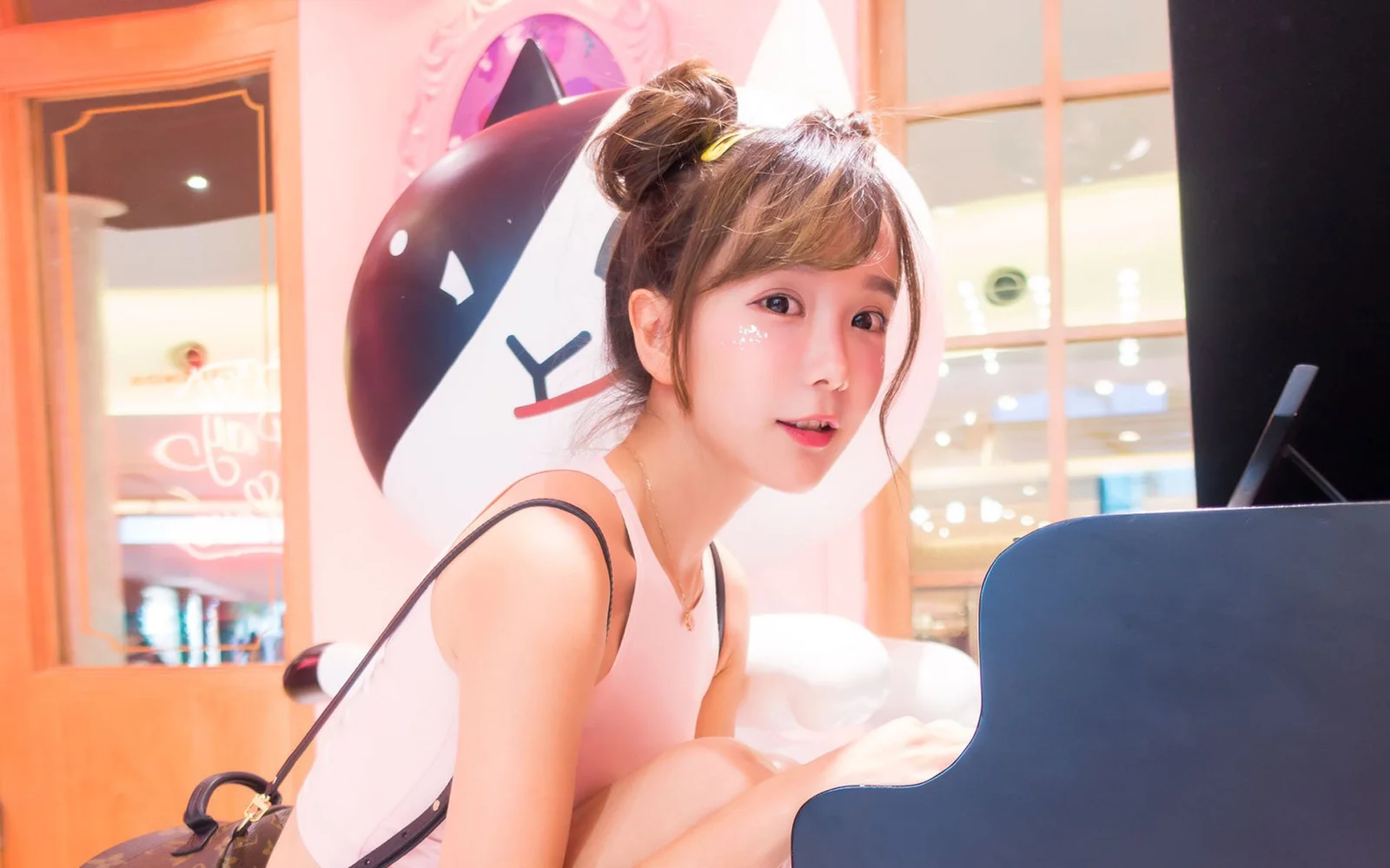 一位女性坐在粉色室内的钢琴旁，面向镜头微笑。