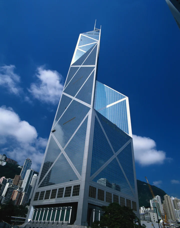 仰拍视角下，一座高耸的玻璃幕墙建筑矗立在蓝天白云与城市高楼之间。