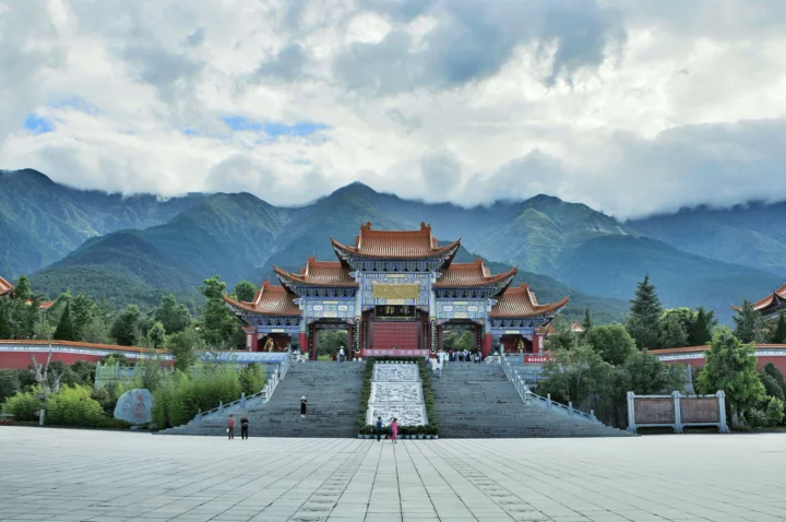 一座传统风格的建筑入口矗立在群山、云层和绿树之间。