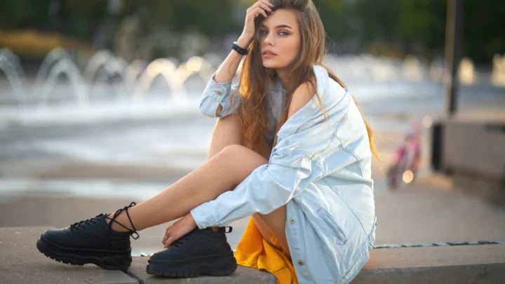 一名成年女子坐在喷泉旁的台阶上，穿着浅色外套和黑色运动鞋。