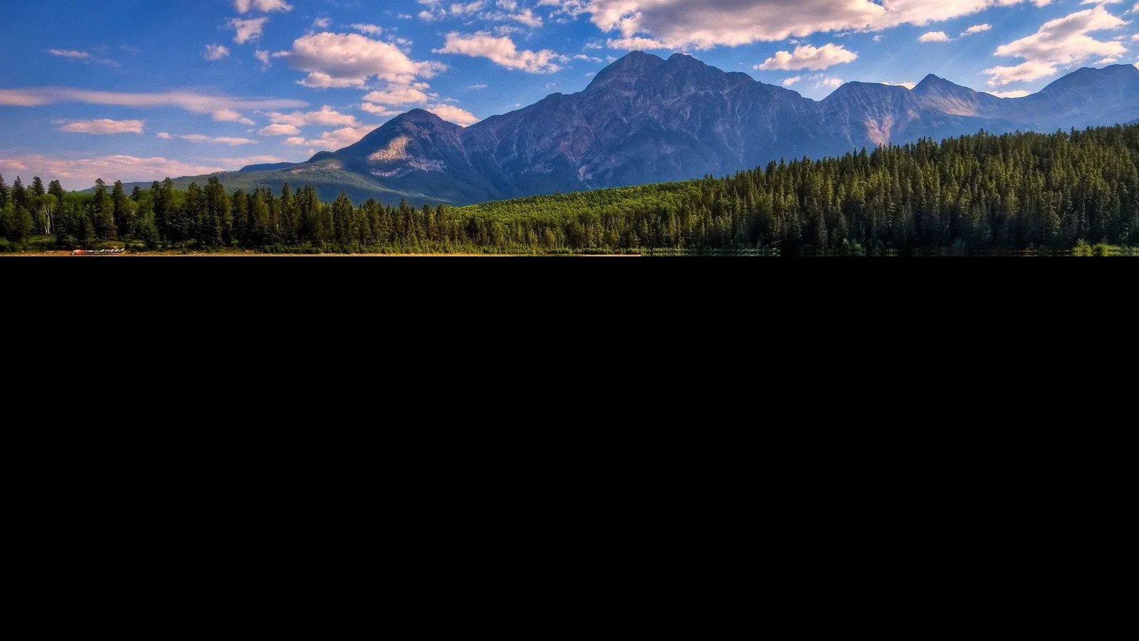 蓝天白云下的山脉、森林与湖面组成风景，画面下方留有大片黑色空白。