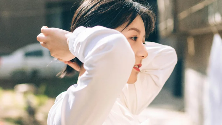 一位身穿白色长袖上衣的女性在明亮的户外光线下整理头发。