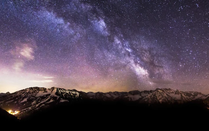 璀璨的银河横跨夜空，下方是被星光映照的雪山山脉。