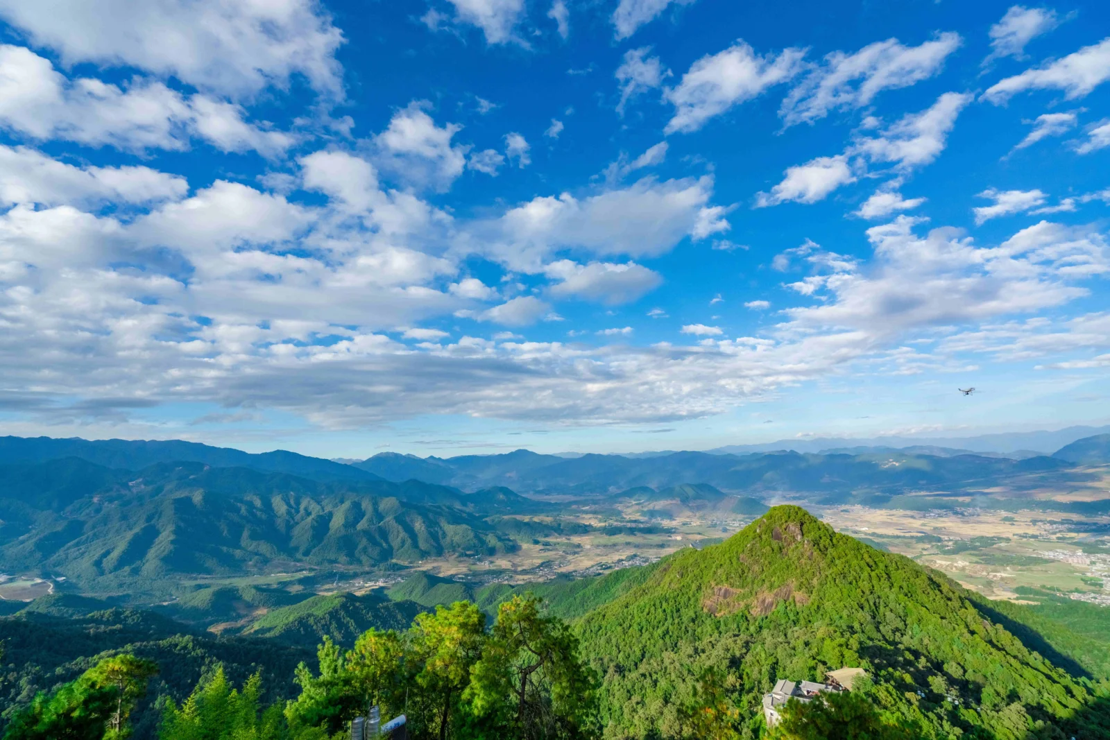 蓝天白云下，层叠山脉环绕着绿色山谷与远处的田野。