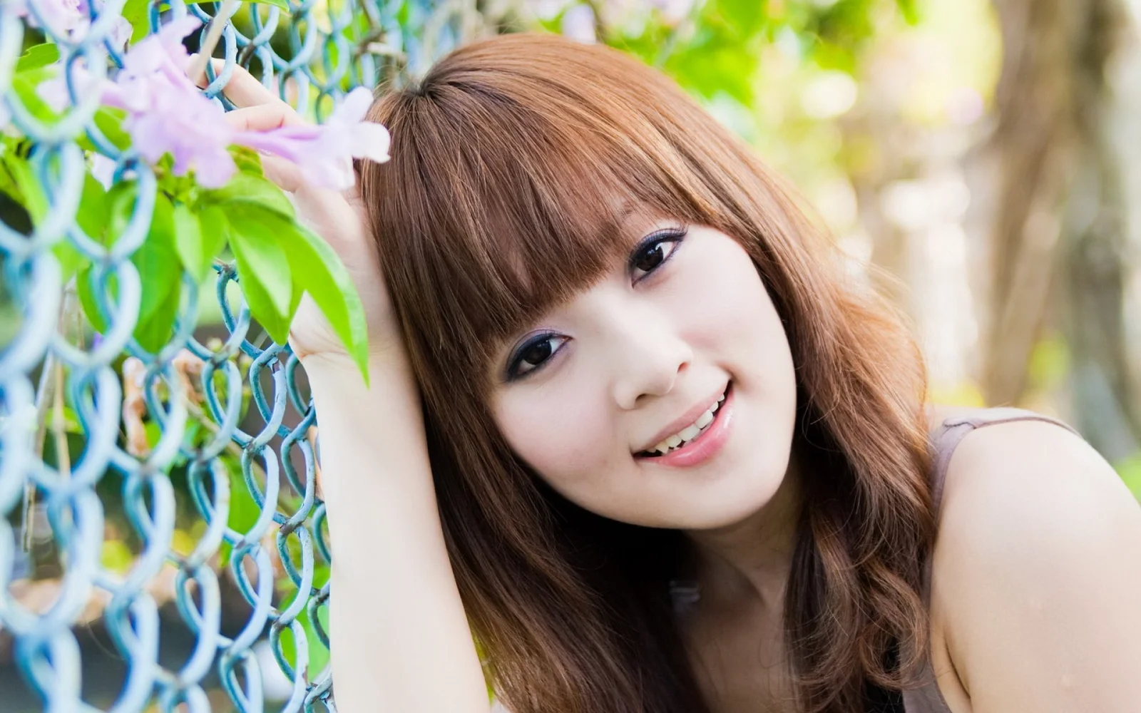 一名长发女子在花朵和绿叶旁对着镜头微笑。