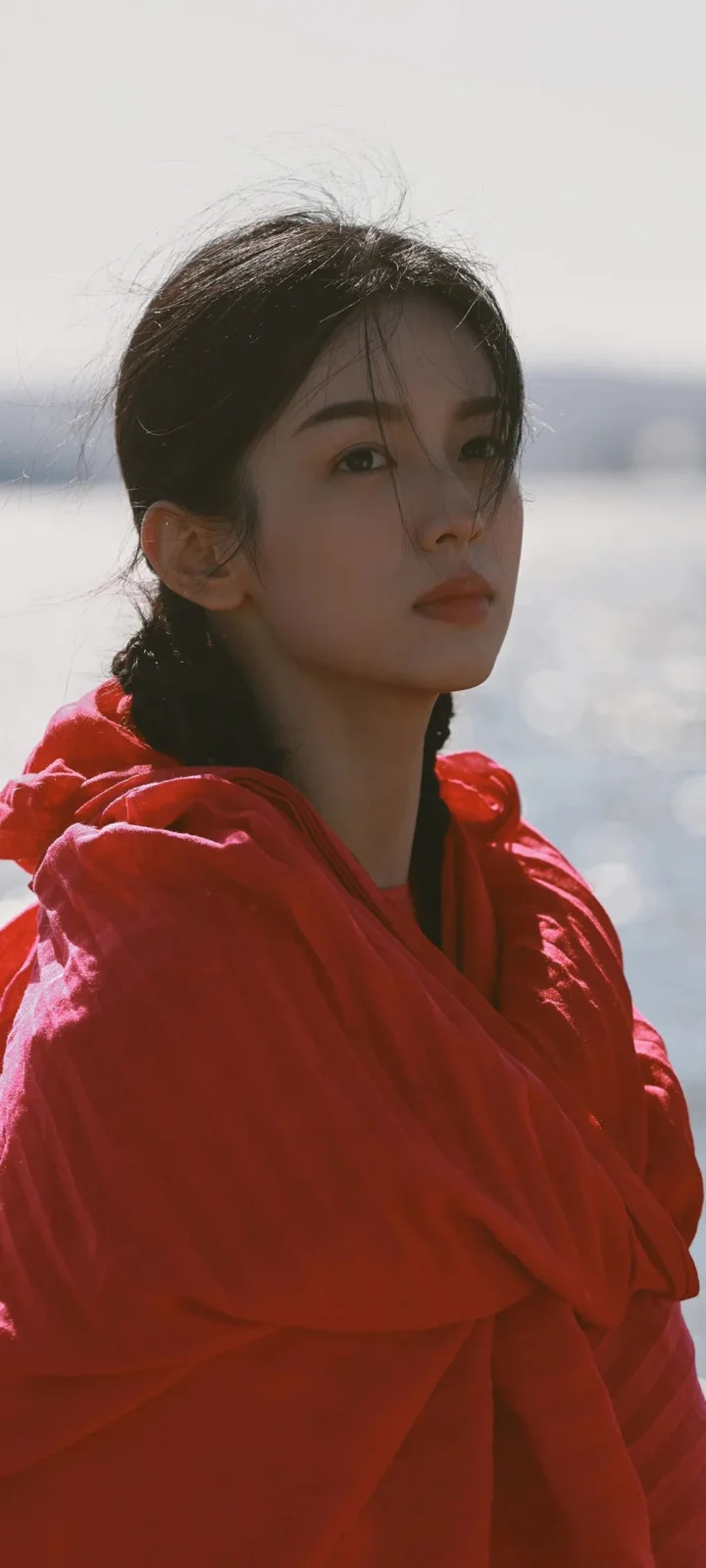 一名身穿红色衣物的女子站在水边，阳光勾勒出她的侧脸轮廓。