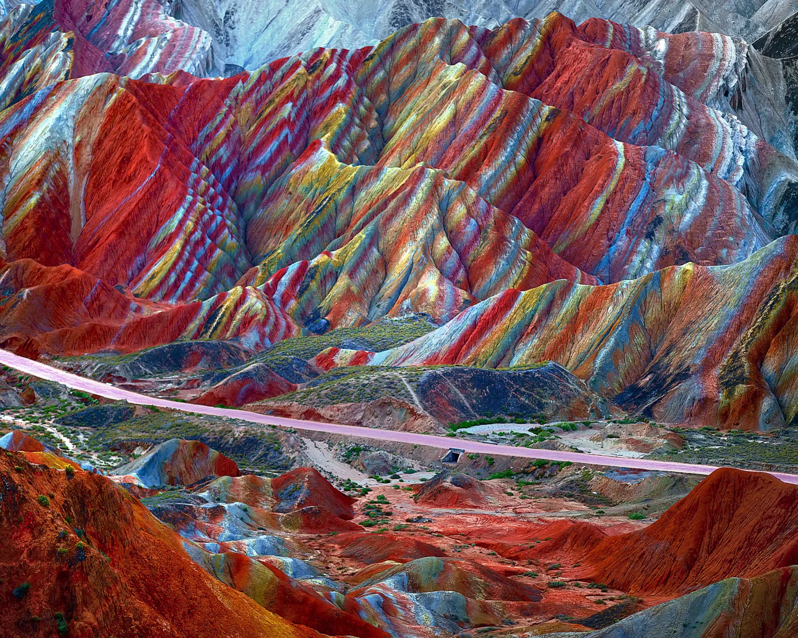 色彩斑斓的山地地貌延伸至远方，山脚下有一条道路穿过荒凉的谷地。