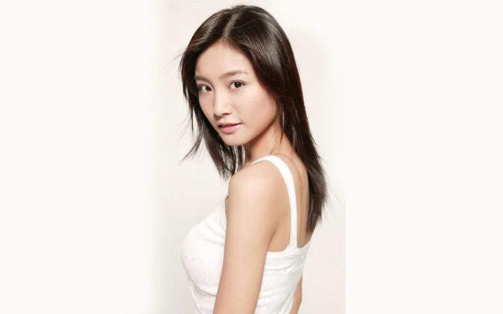 一名成年女性身穿白色无袖上衣，在浅色背景前侧身面向镜头。