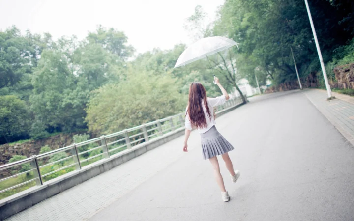 투명한 우산을 든 사람이 비 오는 숲길을 걷고 있습니다.