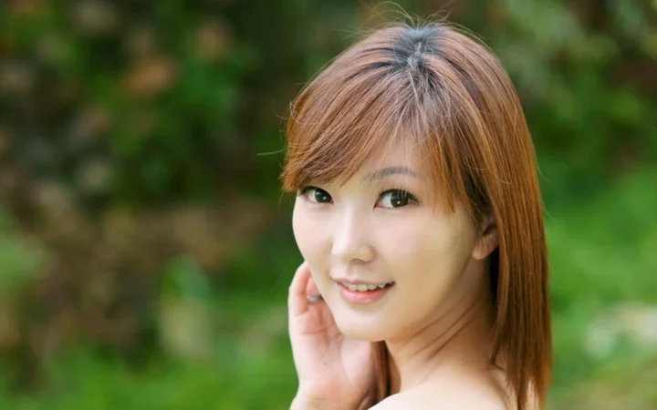 一名棕色长发女性在绿色户外背景前微笑看向镜头。