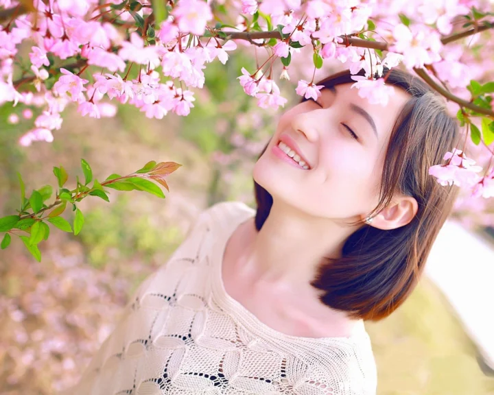一位成年女子在盛开的粉色樱花枝下闭眼微笑。