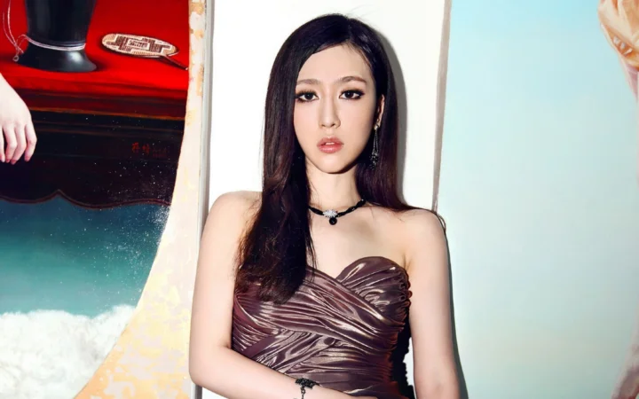 一位長髮女性身穿棕色紋理抹胸禮服，置身於色彩繽紛的背景前。