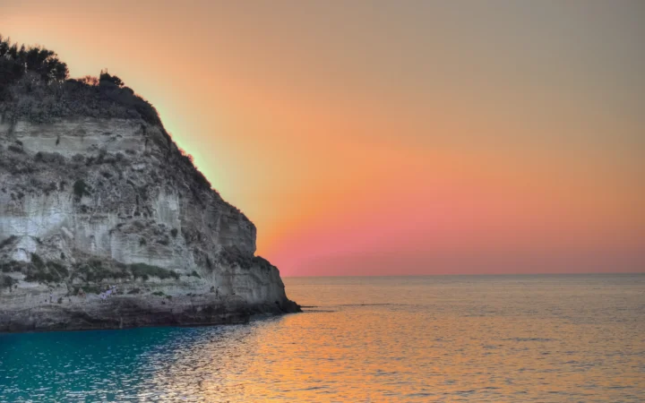 夕阳映照着平静海面，峭壁位于画面左侧。