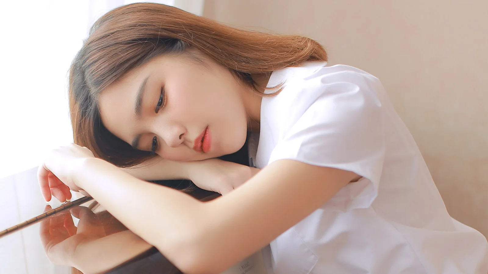 一名穿白色上衣的女子将头枕在桌上的手臂上小憩。