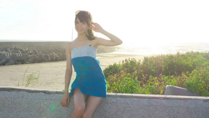 一名女子坐在海边的堤岸上，阳光照亮了海面和周围植被。