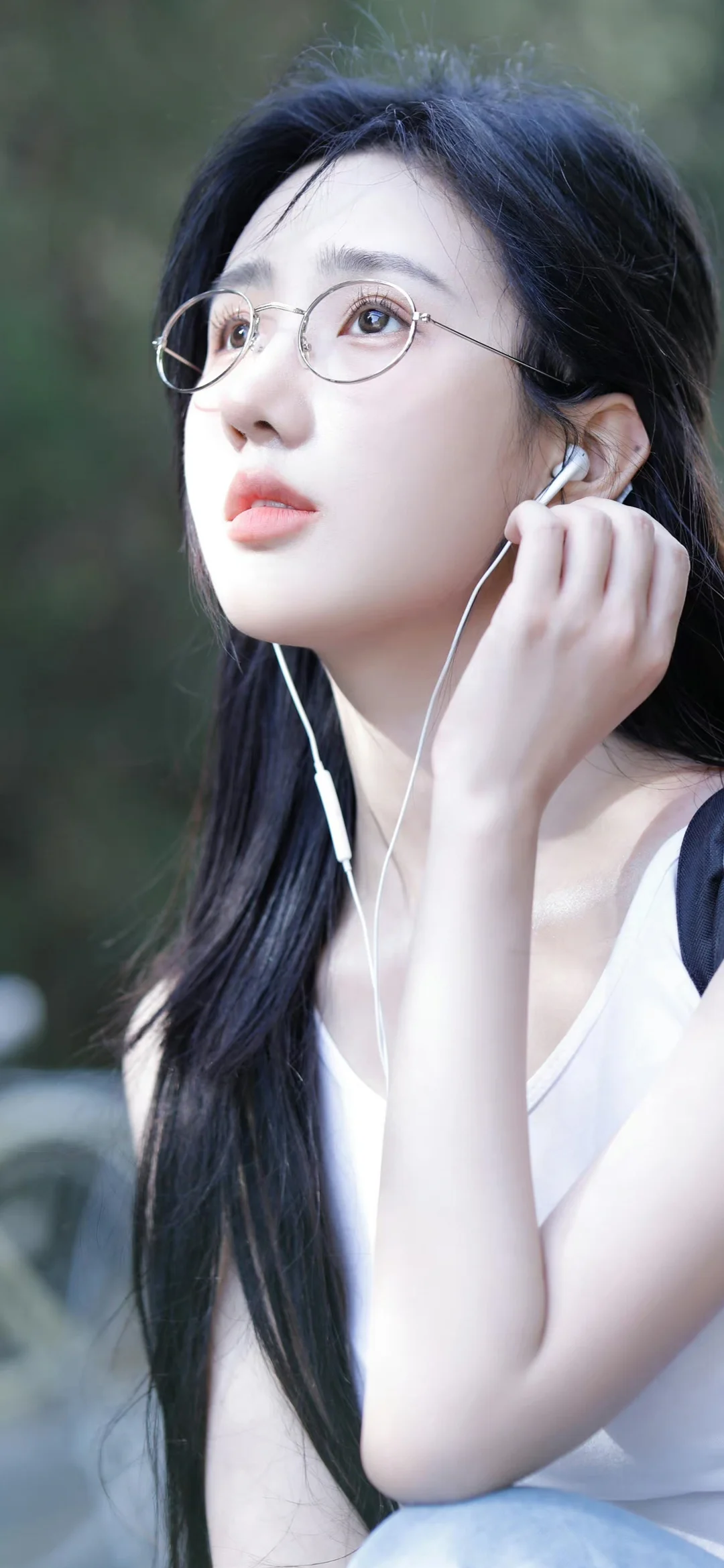 一名戴圆框眼镜、佩戴耳机的长发女子站在户外。