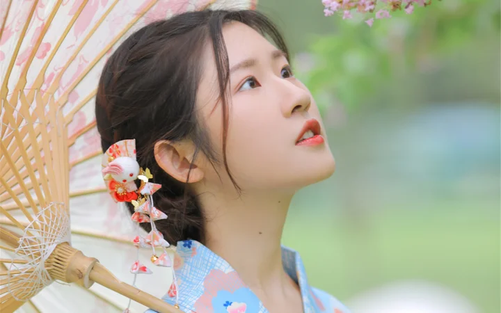 一名女子手持带花纹的扇子，侧脸仰望户外景色。