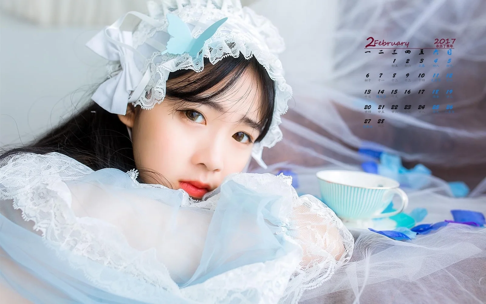 一名成年女性穿着白色蕾丝装扮，靠在室内桌面旁看向镜头。
