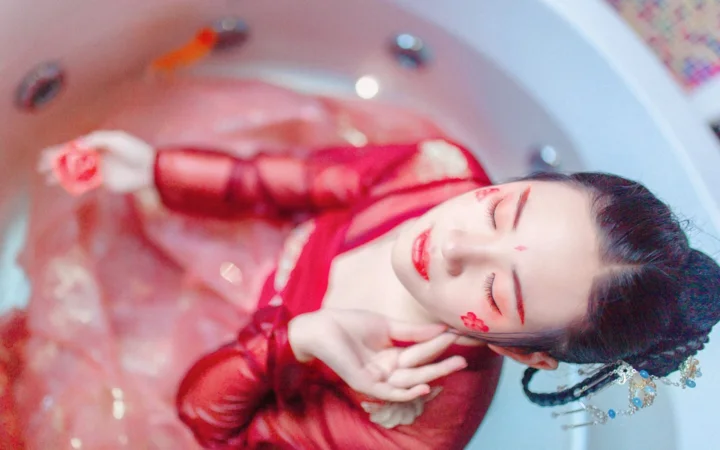 一名身穿红色传统服饰的女性闭着眼睛躺在浅色背景上。