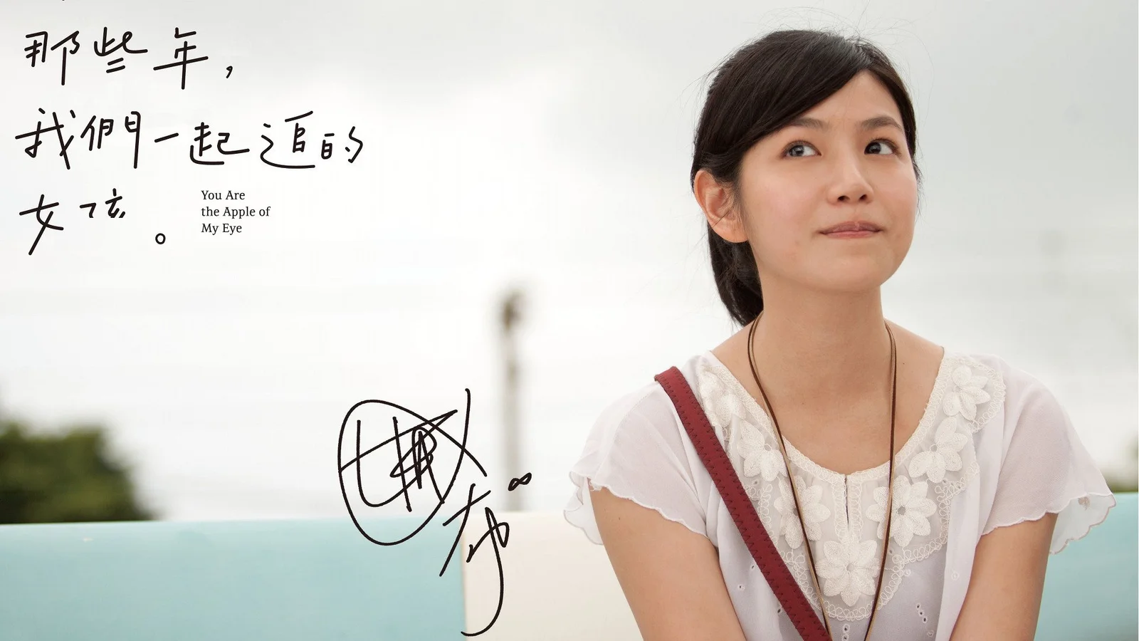 白い服を着た女性が右側に写り、左側に手書きの文字とサインがあります。