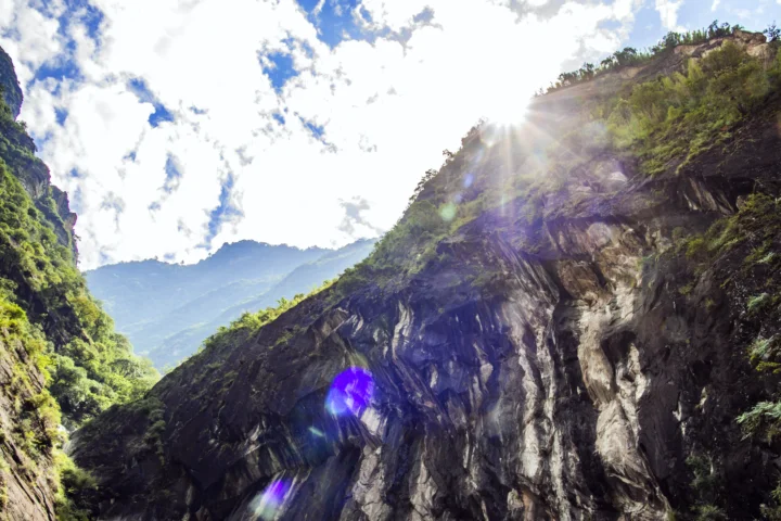 阳光穿过云层照亮了森林覆盖的山谷与陡峭岩壁。