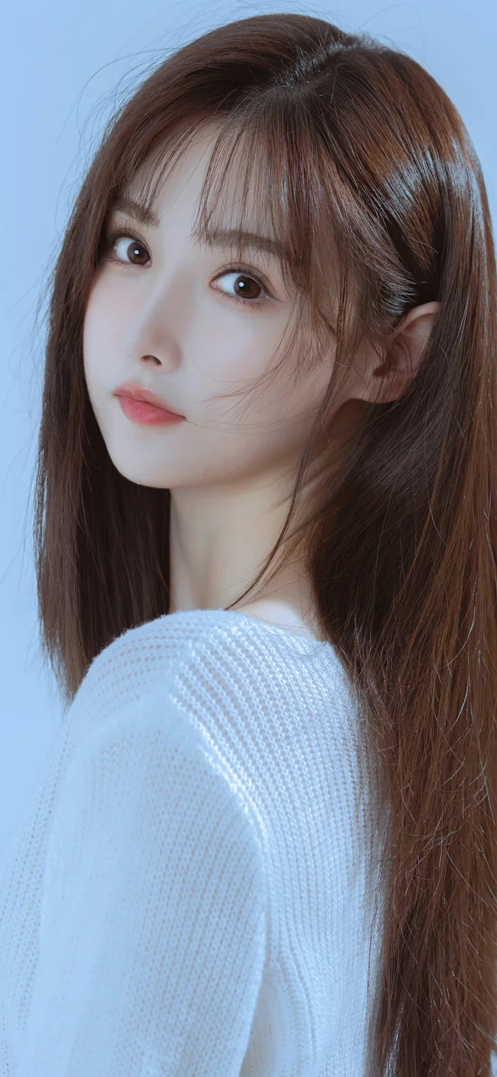 一名棕色长发女性穿着白色针织衫，在浅蓝色背景前回眸看向镜头。