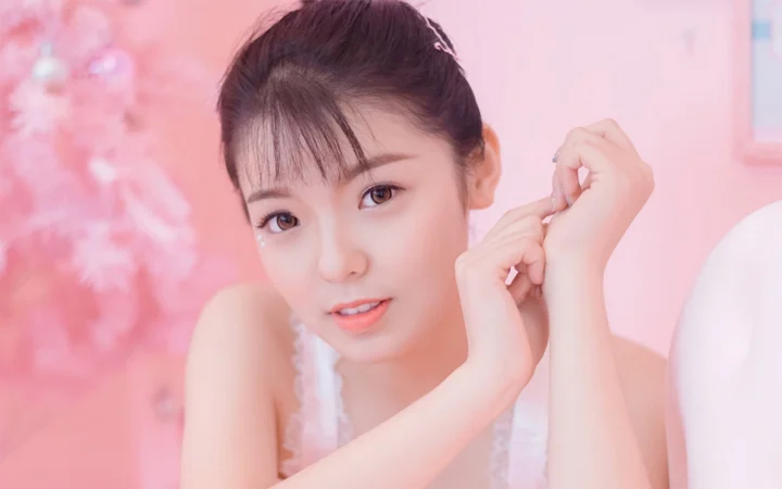 분홍빛 배경 앞에서 성인 여성이 카메라를 바라보는 부드러운 인물 사진입니다.