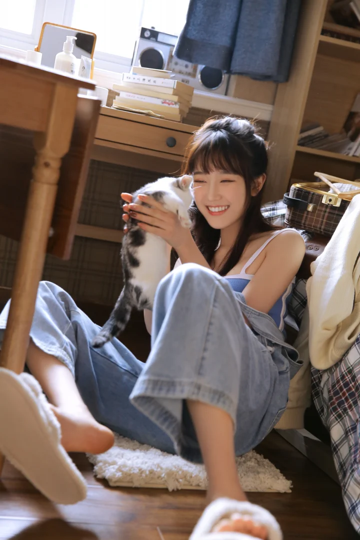 一名成年女子坐在室内地板上微笑着抱着一只猫。