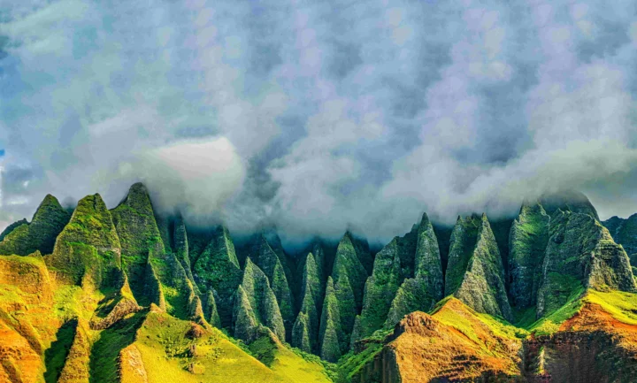 葱郁的尖峭山峰延伸在画面中，山顶被厚重云雾笼罩，前景沐浴在金色阳光下。