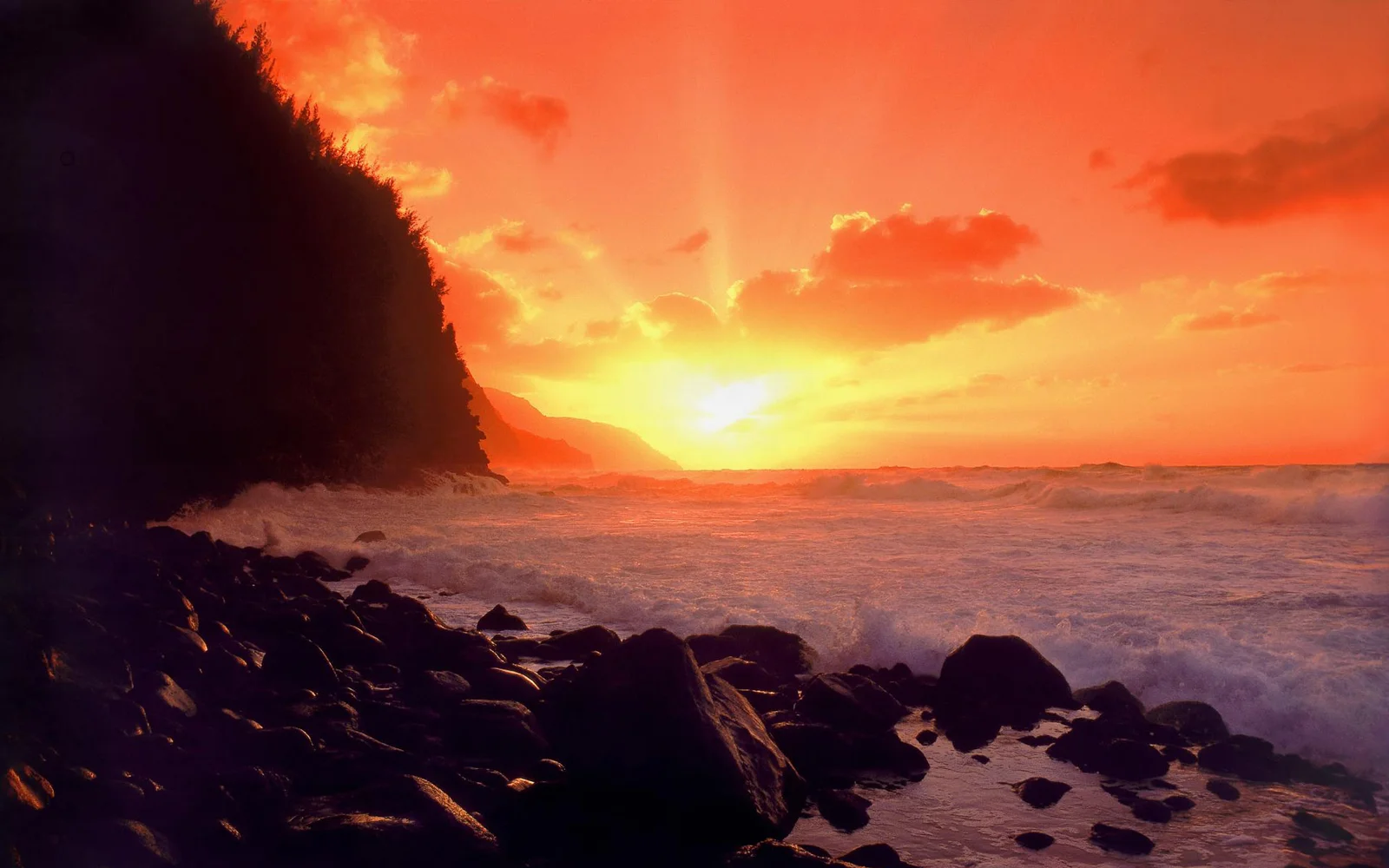 夕陽映照著海面、岩石海灘和左側的深色海岸懸崖。