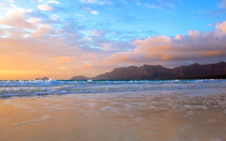 晚霞映照下的海滩、层叠海浪与远处山脉构成宁静的自然风景。