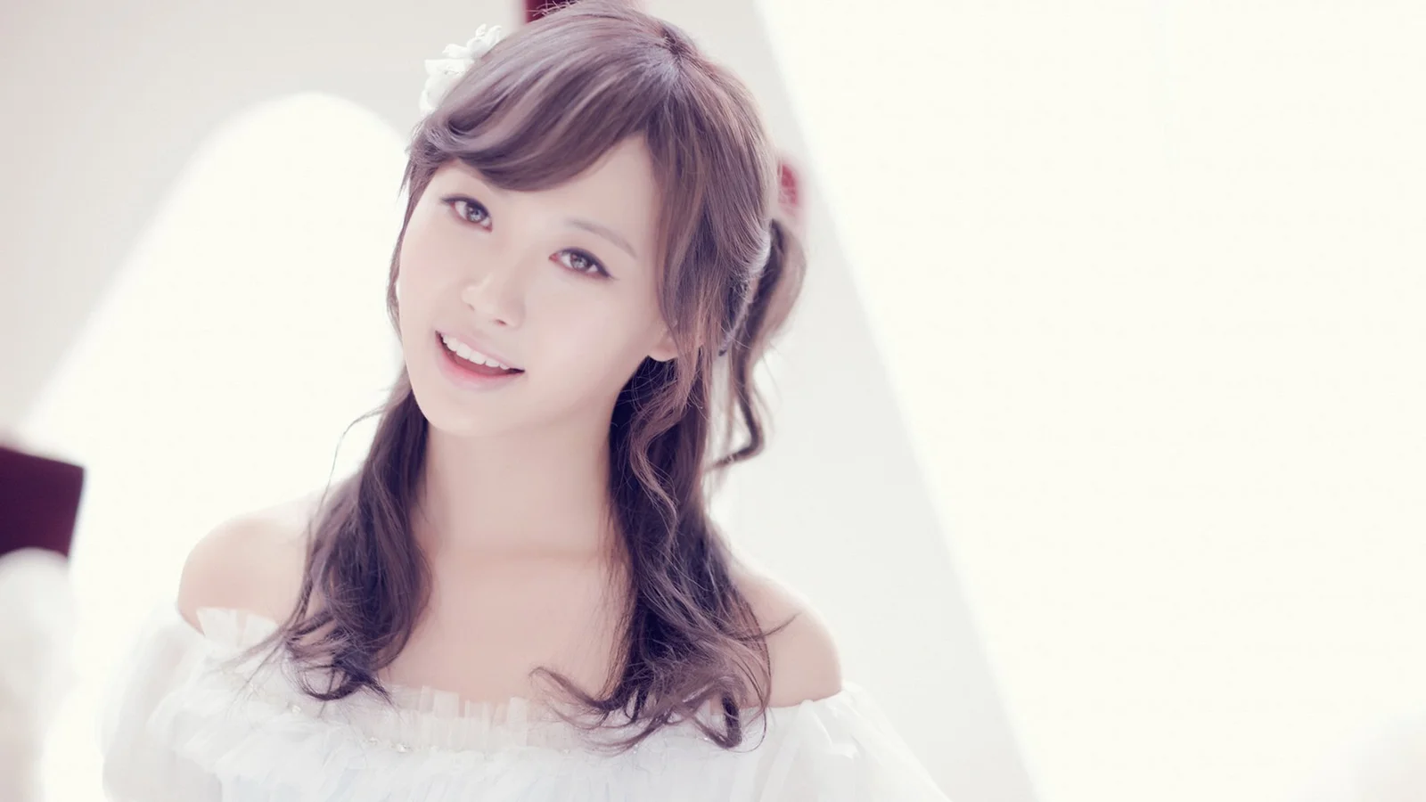 부드럽고 밝은 배경 앞에서 성인 여성이 카메라를 향해 미소 짓고 있다.