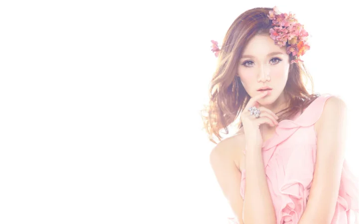 花飾りを身につけ、ピンクのドレスを着た女性が白い背景の前でポーズを取っています。