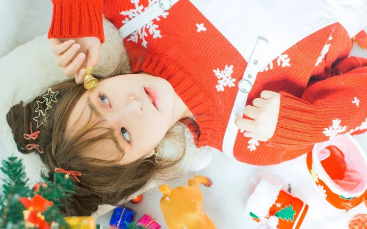 一名成年女性穿着红色雪花毛衣，躺在圣诞装饰旁看向镜头。