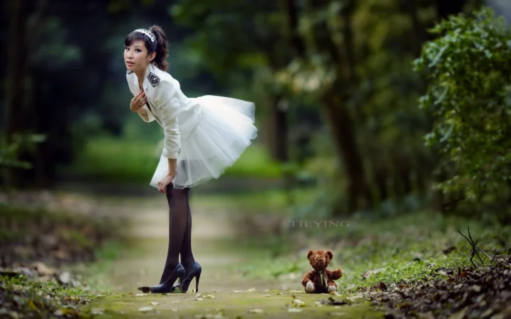白い服を着た女性が、緑の木々と草に囲まれた森の小道に立っています。