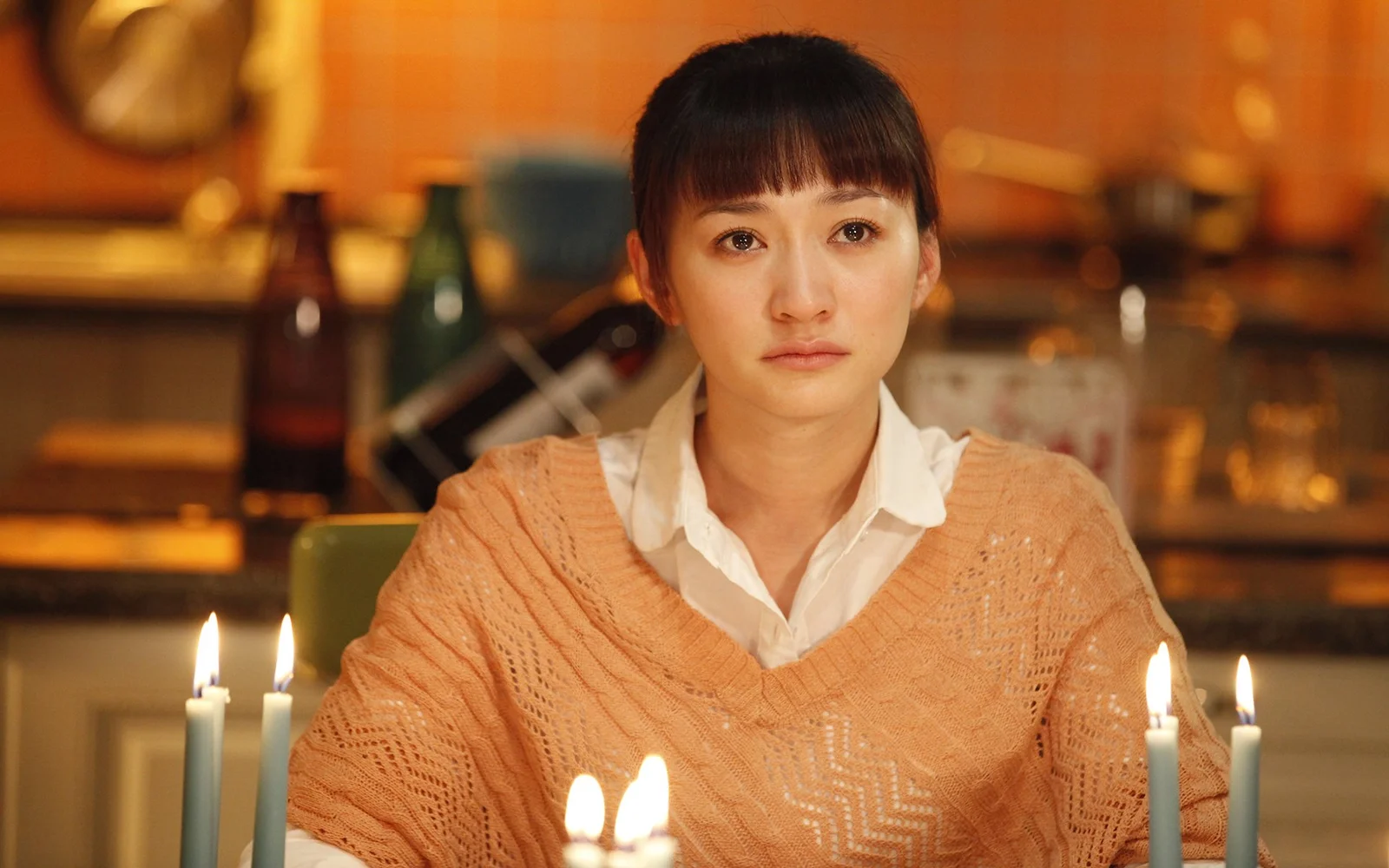 따뜻한 조명과 촛불이 비치는 레스토랑에 성인 여성이 앉아 있습니다.