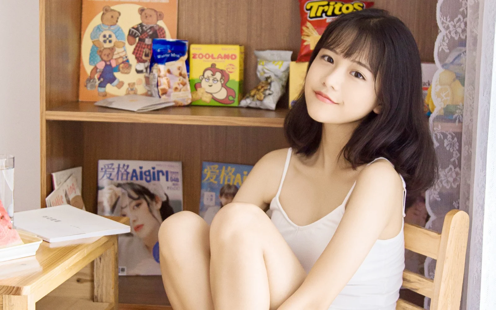 一名女子坐在木质书架旁，对着镜头微笑。
