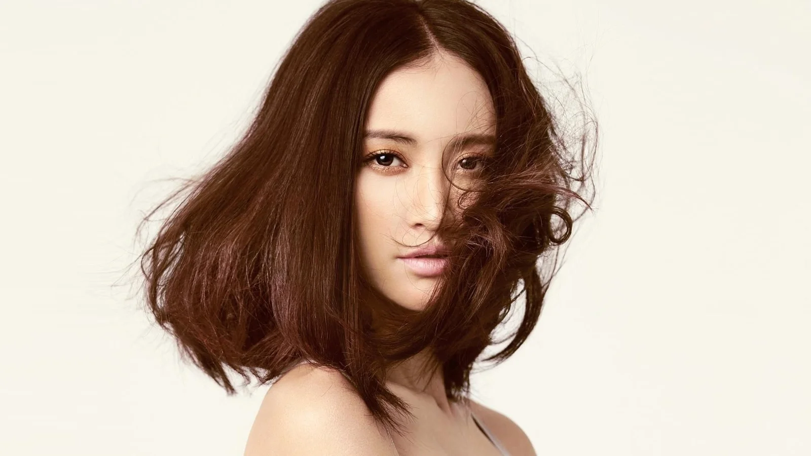 一名棕色中长发女性在浅色背景前侧身凝视镜头。