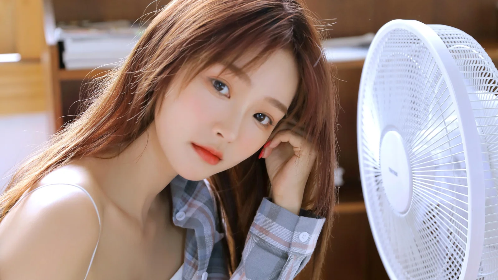 갈색 긴 머리의 여성이 실내에서 흰색 선풍기 옆에 있는 인물 사진입니다.