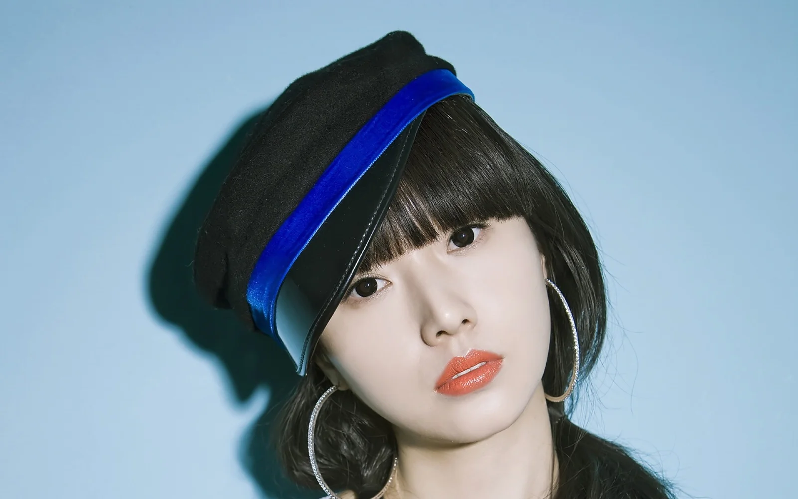 검정과 파란색 베레모를 쓴 여성이 연한 파란색 배경 앞에서 카메라를 바라보고 있다.