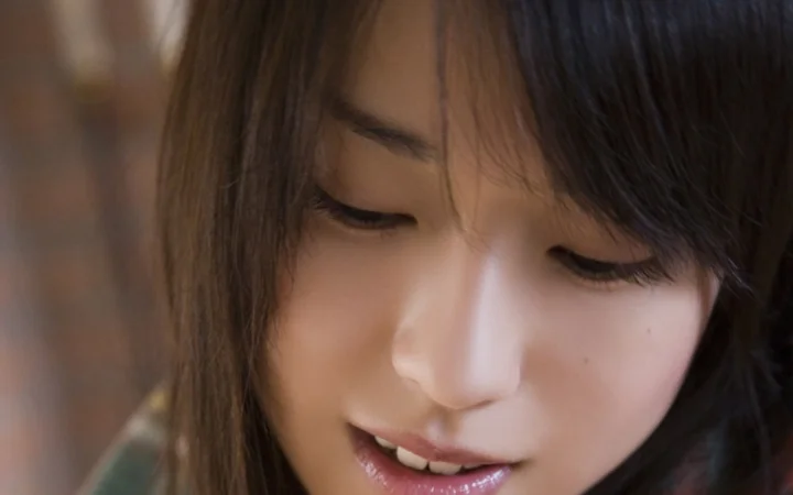 黒髪の女性が穏やかな笑みを浮かべながら下を向いているクローズアップポートレートです。