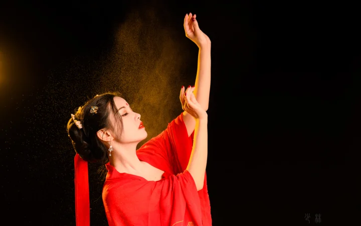 一名身穿红色服装的女子在黑色背景前抬起双臂。
