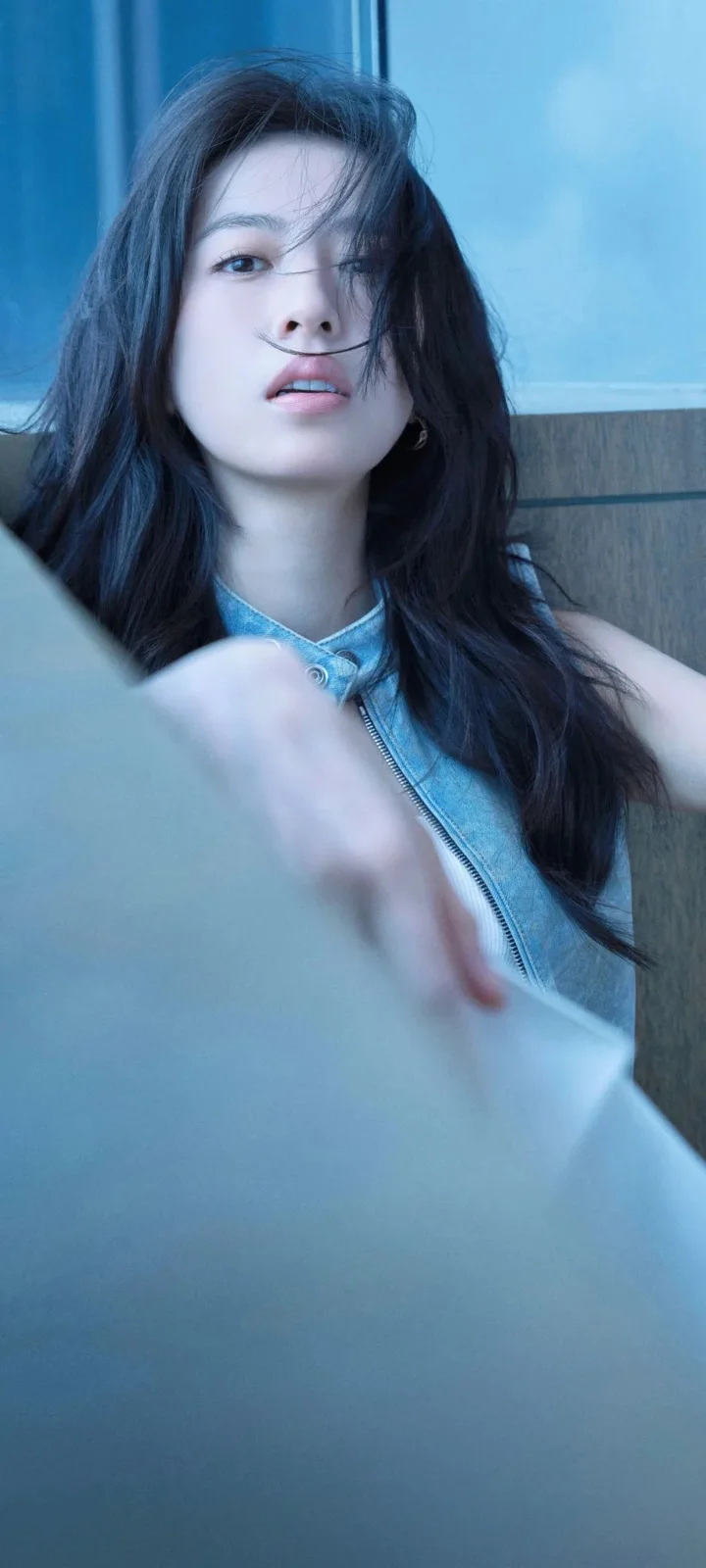 一名长发女子身穿无袖牛仔上衣，在蓝色光线下靠近镜头。