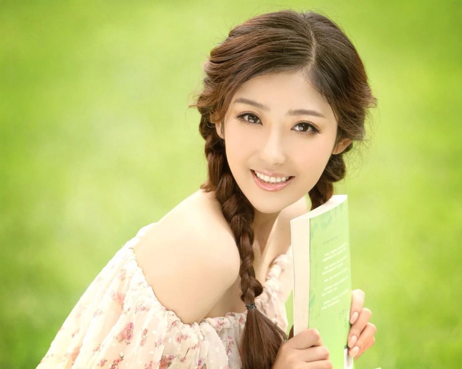 밝은 초록색 배경 앞에서 미소 짓는 성인 여성이 초록색 책을 들고 있습니다.