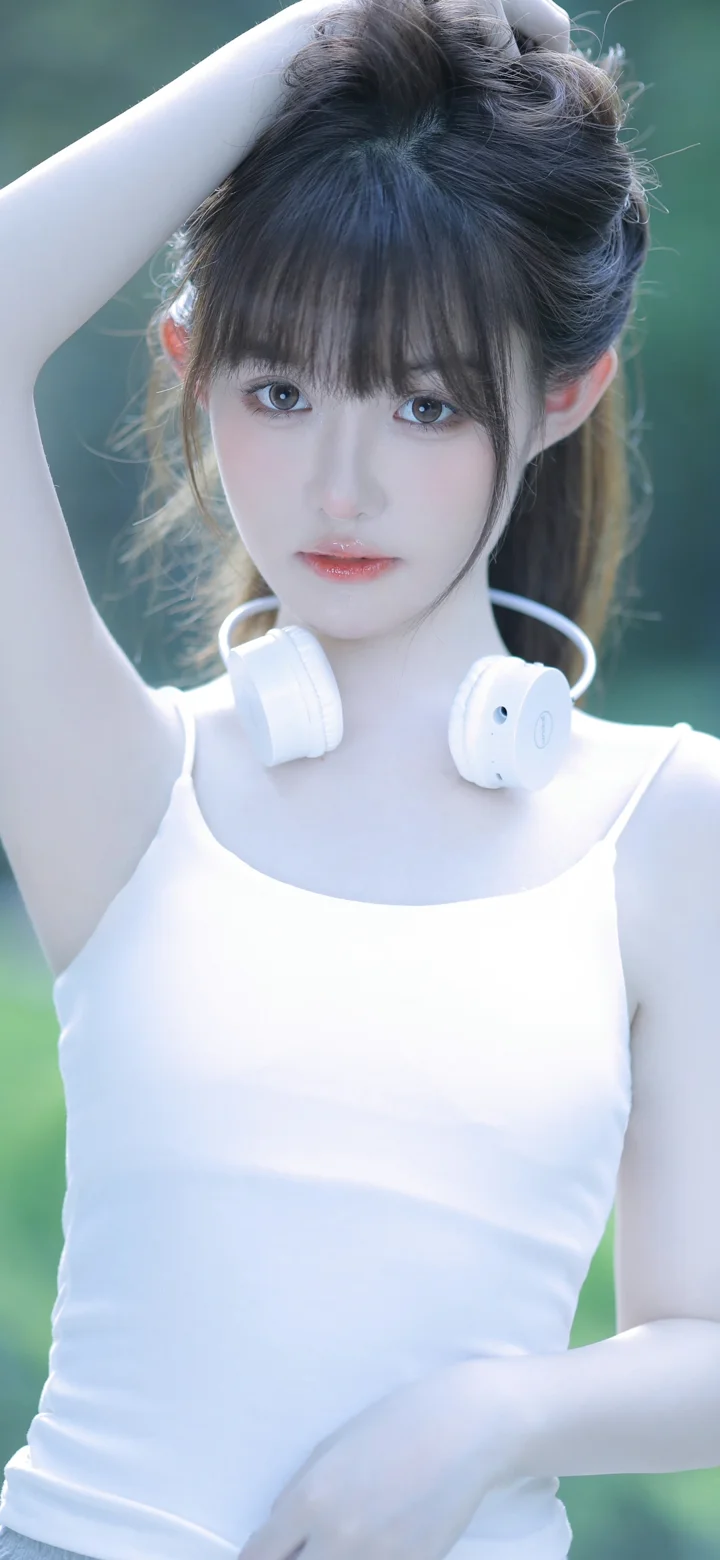 一名身穿白色背心的女性戴着白色头戴式耳机，面对镜头摆姿势。