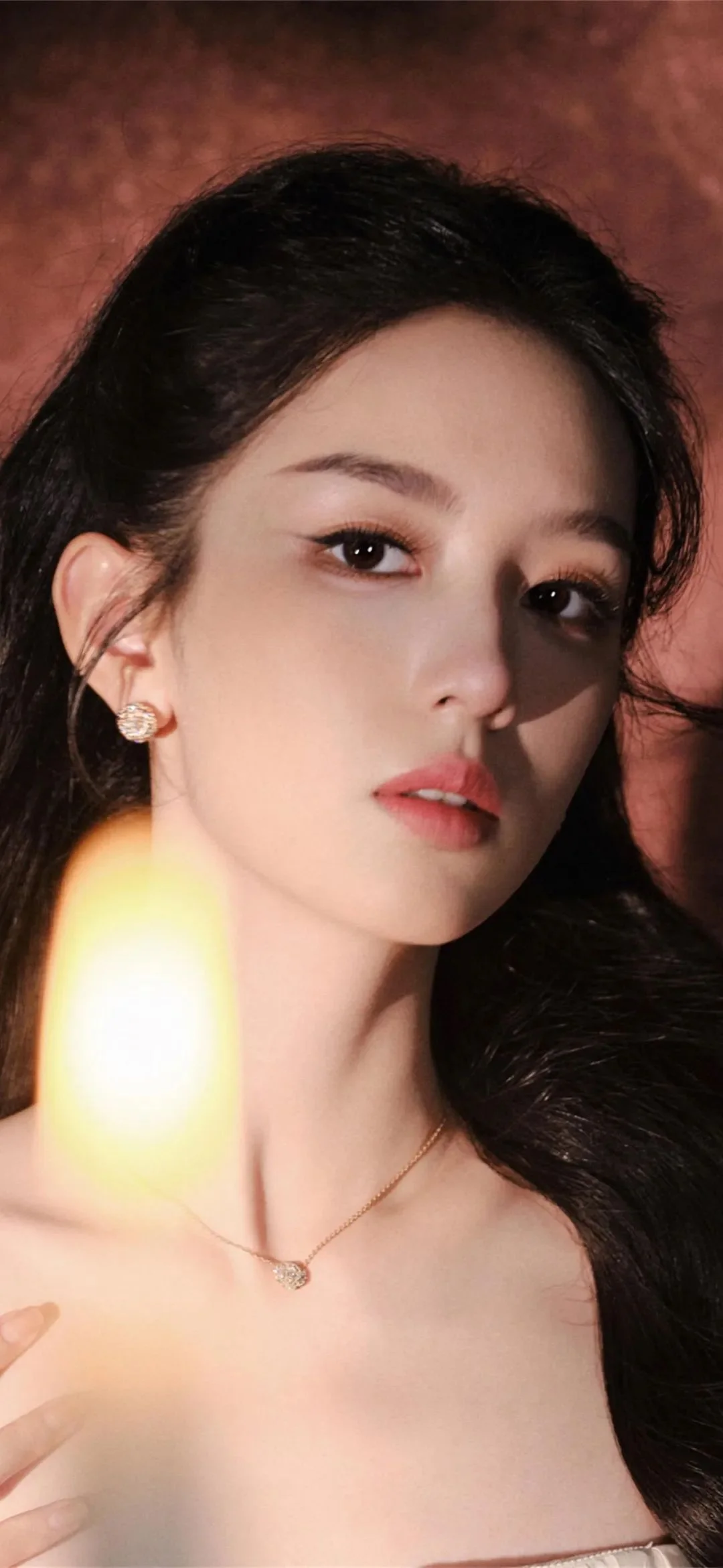따뜻한 색조의 배경 앞에서 카메라를 바라보는 성인 여성의 얼굴을 부드러운 명암으로 담은 클로즈업 인물 사진이다.
